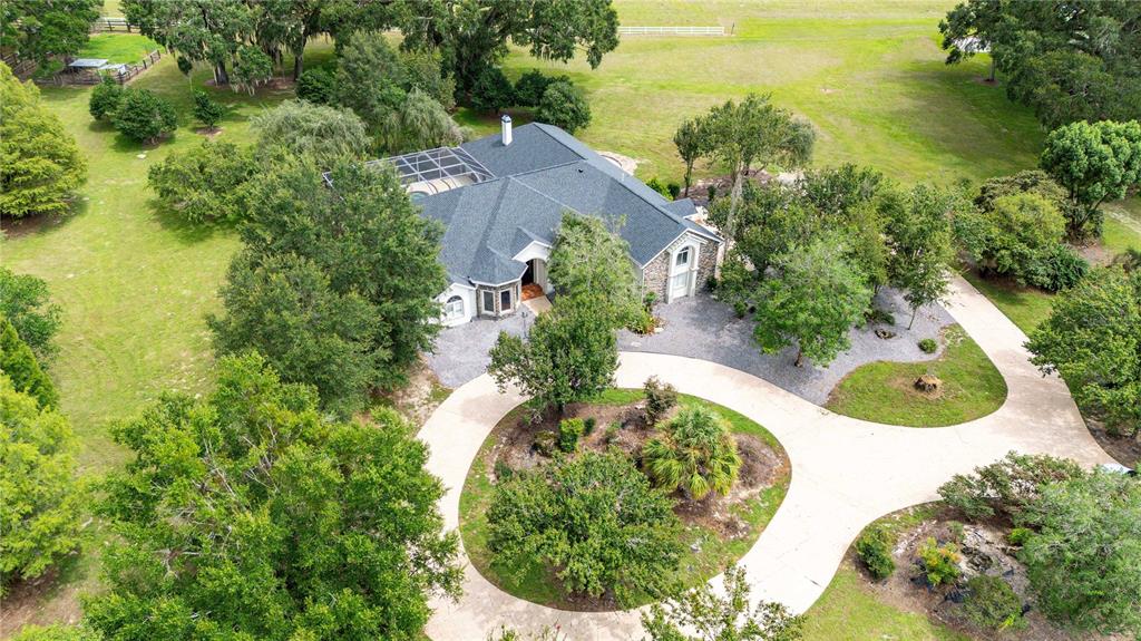 An aerial view shows a house with a dark roof, pool enclosure, and circular driveway — 17401 S HIGHWAY 475, SUMMERFIELD, FL