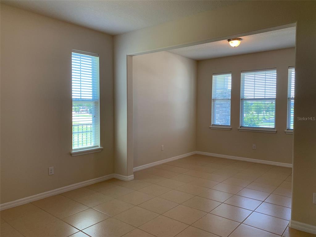 An empty room with beige tile flooring, neutral walls, and several windows with blinds — 2860 CHANTILLY AVENUE, KISSIMMEE, FL