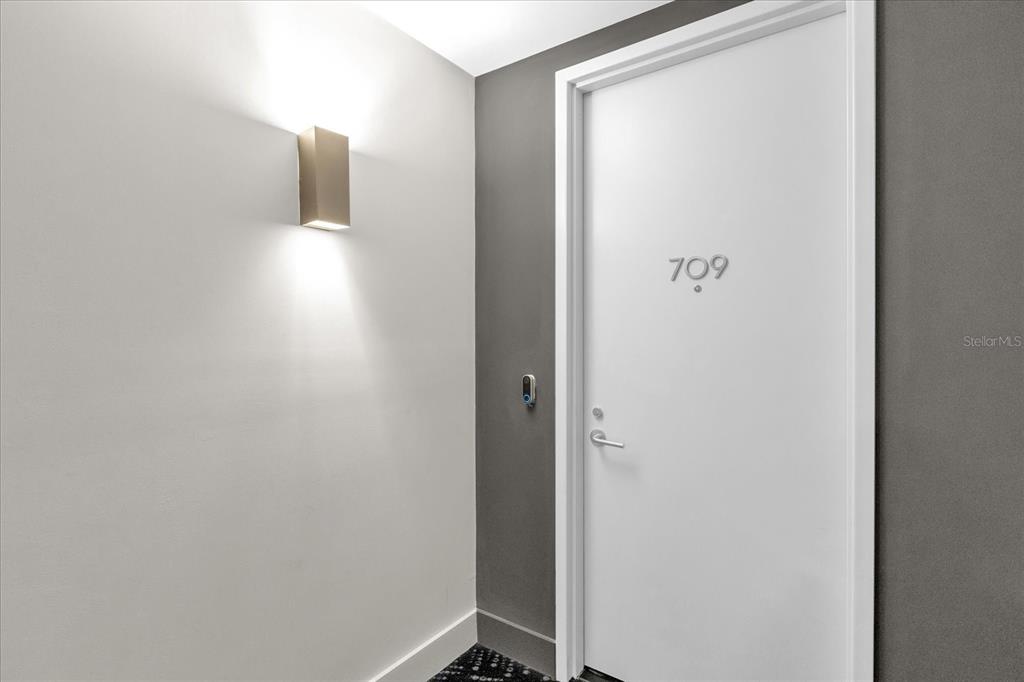 A white door labeled 709 sits next to a wall sconce in a hallway — 260 S OSCEOLA AVENUE UNIT 709, ORLANDO, FL