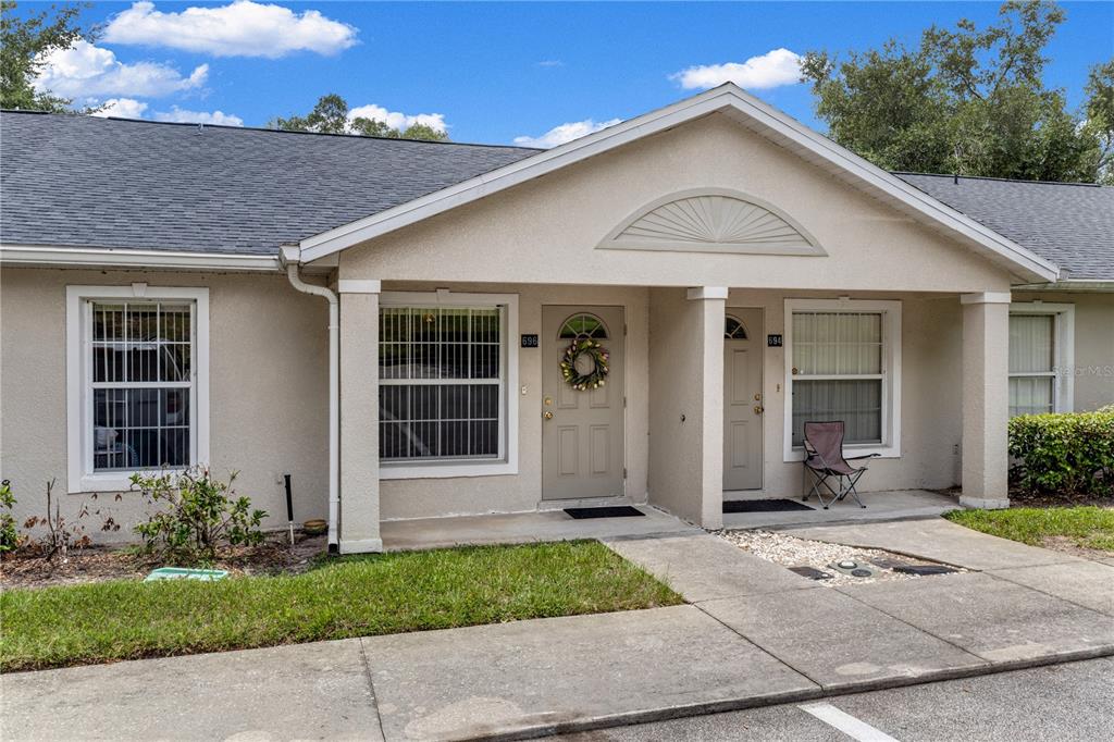 The exterior of a single-story duplex features beige stucco walls, gray shingled roofs, and two entrances — 696 S GRAND HIGHWAY, CLERMONT, FL