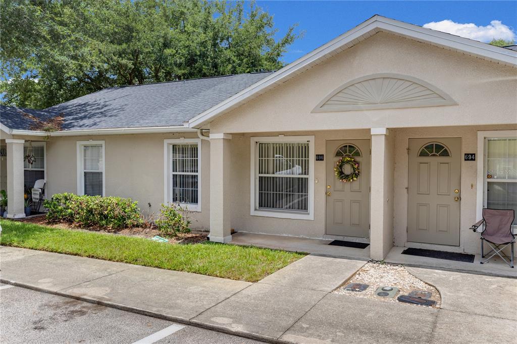 A beige single-story duplex with two front doors, windows, and a small patch of landscaping — 696 S GRAND HIGHWAY, CLERMONT, FL