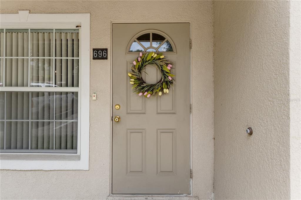A beige front door with a floral wreath and a window with blinds to the left — 696 S GRAND HIGHWAY, CLERMONT, FL