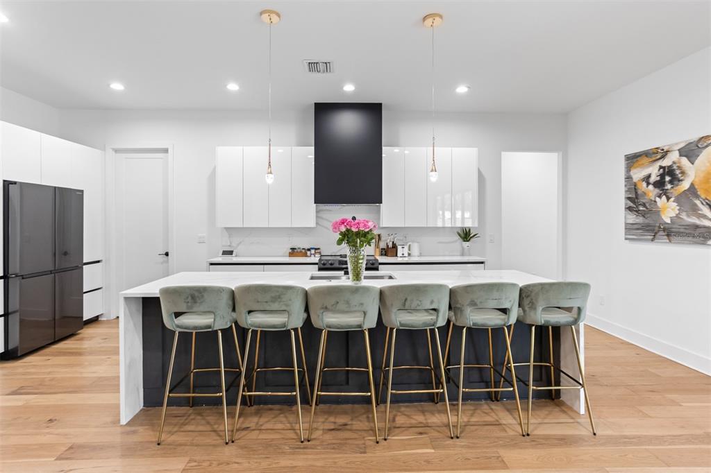 A modern kitchen features a large island with six velvet stools, white cabinets, and dark accents — 3306 W VAN BUREN DRIVE, TAMPA, FL