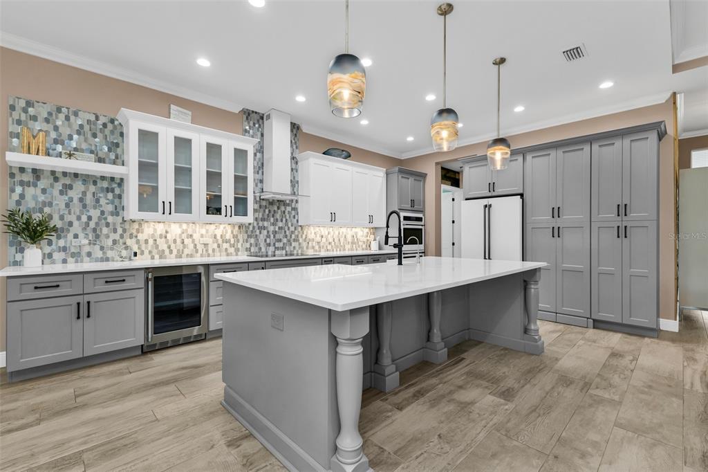 A modern kitchen features a large gray island, white upper cabinets, and a tiled backsplash — 28975 SMUGGLERS LANE, PUNTA GORDA, FL