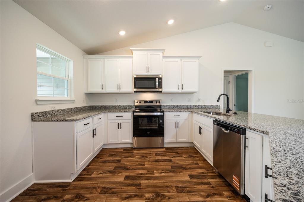 A bright dining nook features a bay window, a modern chandelier, and wood-look flooring — 21 RICHMOND DRIVE, PALM COAST, FL
