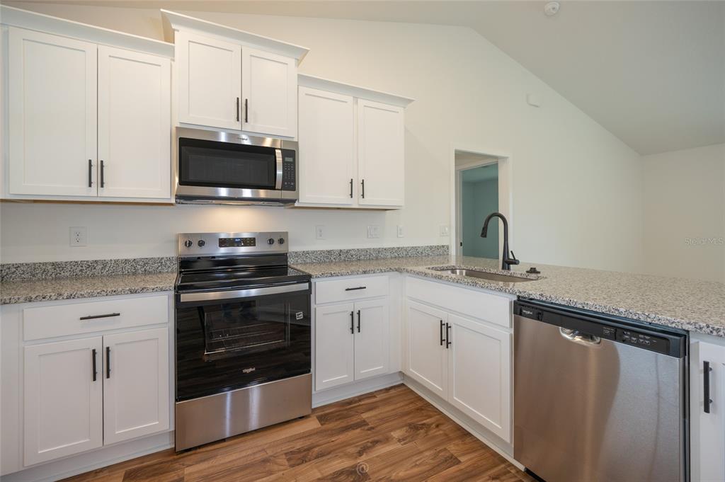 An open-concept kitchen with wood cabinets and a living area with carpet and vaulted ceilings — 21 RICHMOND DRIVE, PALM COAST, FL