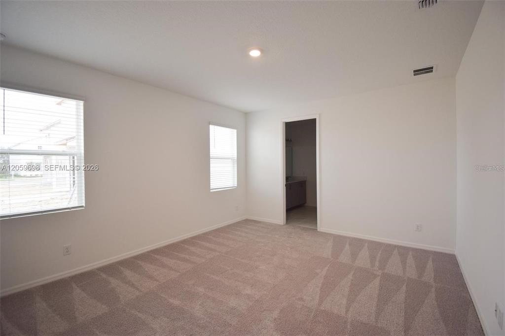 An empty bedroom features beige carpet, white walls, two windows with blinds, and an attached bathroom — 2370 LANCASHIRE STREET, DAVENPORT, FL
