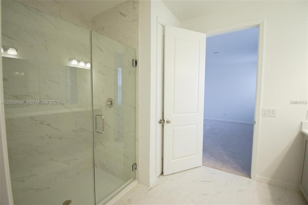 A bathroom features a glass-enclosed walk-in shower with white marble-look tile and an open doorway — 2370 LANCASHIRE STREET, DAVENPORT, FL