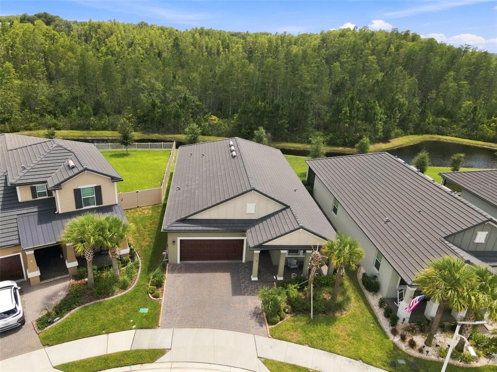 An aerial view shows three suburban houses with dark metal roofs and paved driveways — 17254 MANGO SHAY COURT, LAND O LAKES, FL