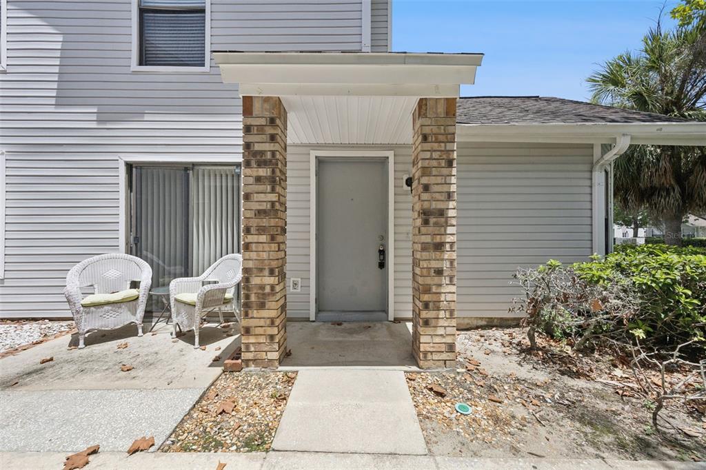 The exterior of a house features a brick-columned entryway, light gray siding, and two chairs — 3023 RIO GRANDE TRAIL UNIT 3023, KISSIMMEE, FL
