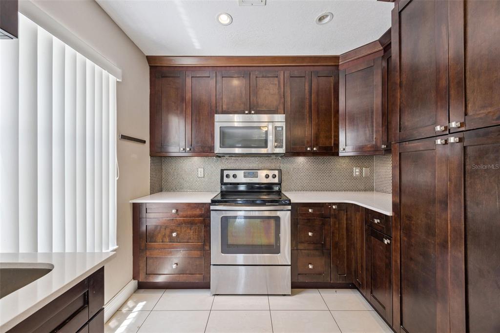 A kitchen features dark wood cabinets, stainless steel appliances, white countertops, and a mosaic tile backsplash — 3023 RIO GRANDE TRAIL UNIT 3023, KISSIMMEE, FL