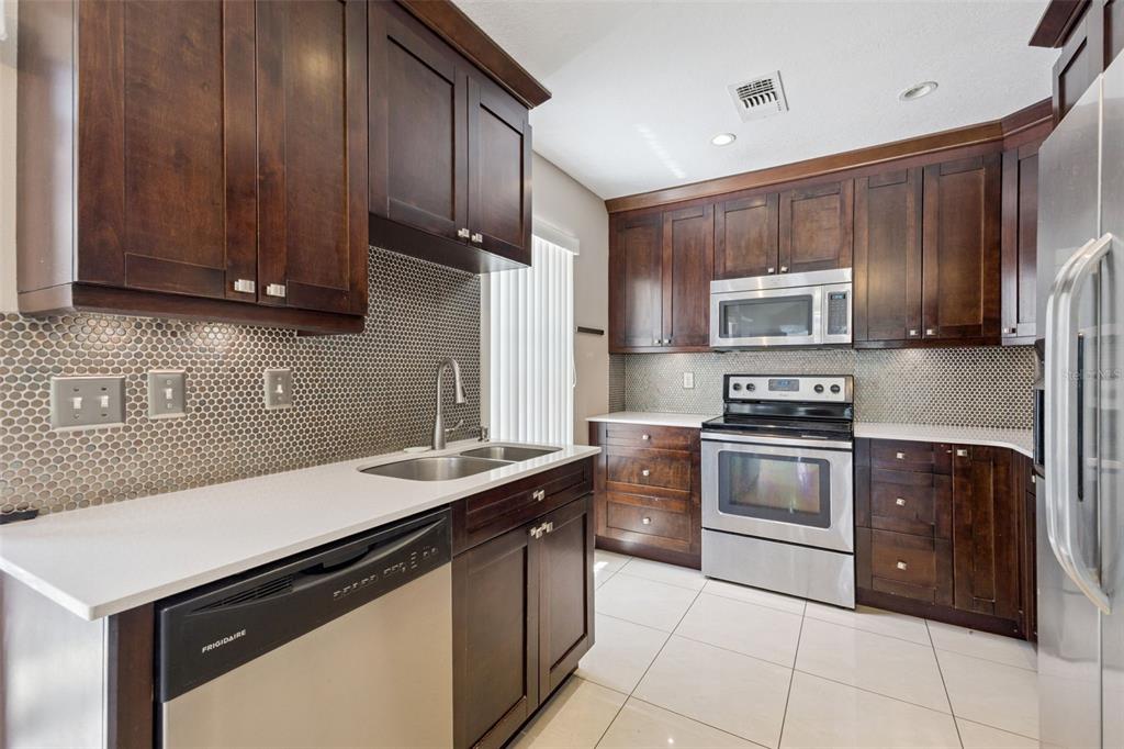 A kitchen features dark wood cabinets, stainless steel appliances, white countertops, and a penny tile backsplash — 3023 RIO GRANDE TRAIL UNIT 3023, KISSIMMEE, FL