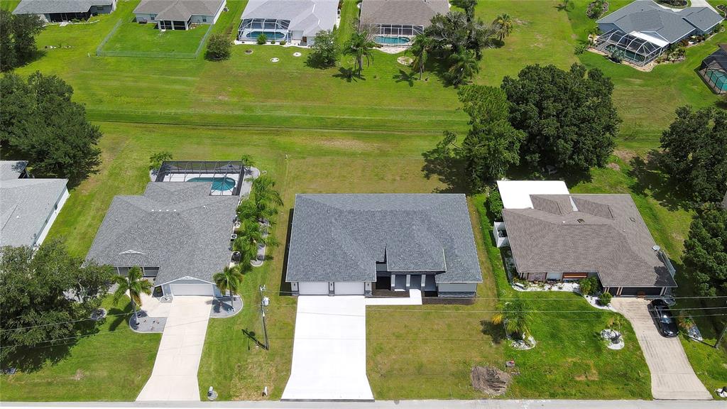 An aerial view shows three suburban houses with driveways and lawns on a residential street — 26082 PAYSANDU DRIVE, PUNTA GORDA, FL