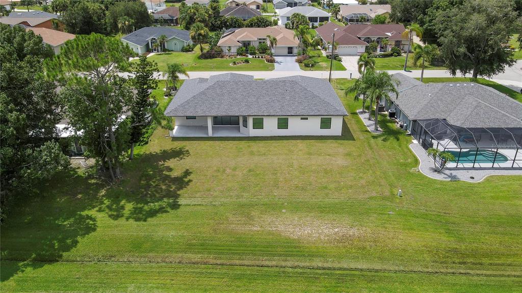 An aerial view shows the back of a single-story house with a large grassy yard — 26082 PAYSANDU DRIVE, PUNTA GORDA, FL