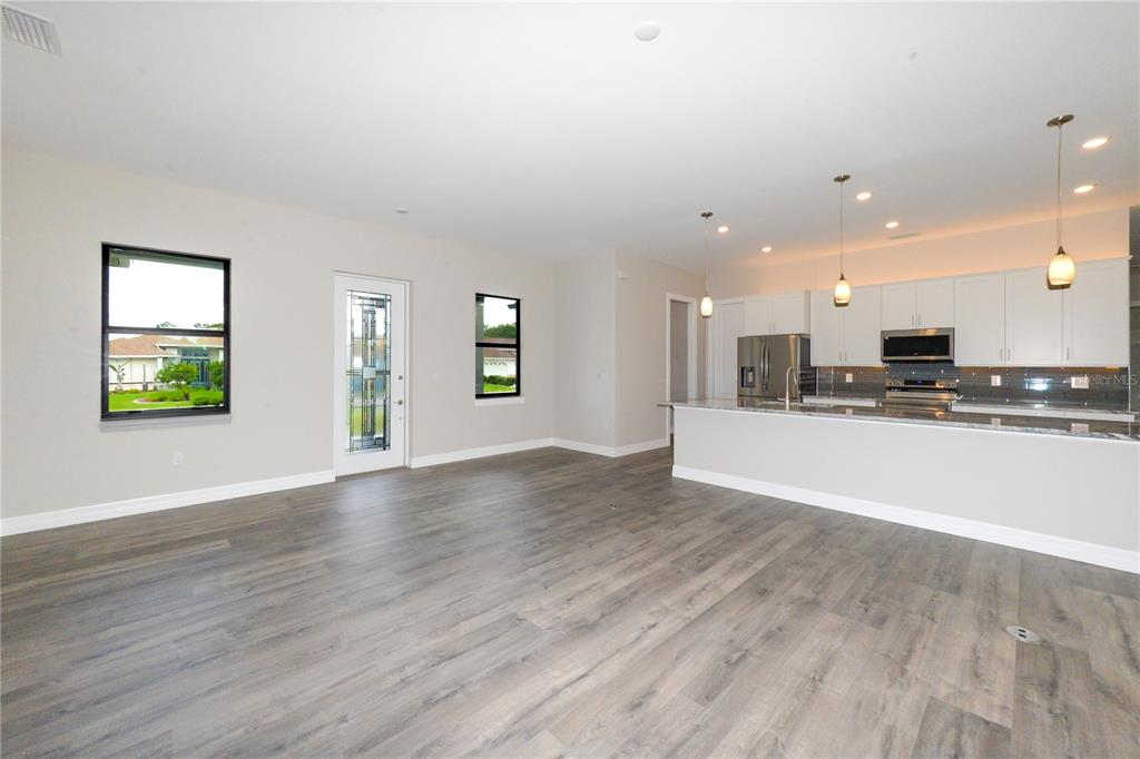 An open-concept kitchen and living area with light-colored walls and wood-look flooring — 26082 PAYSANDU DRIVE, PUNTA GORDA, FL