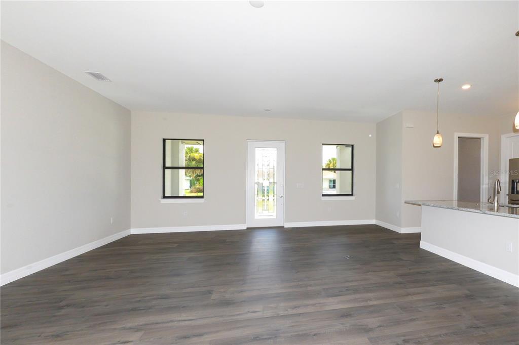 This open-concept living area features dark wood-look flooring, neutral walls, and a kitchen island — 26082 PAYSANDU DRIVE, PUNTA GORDA, FL