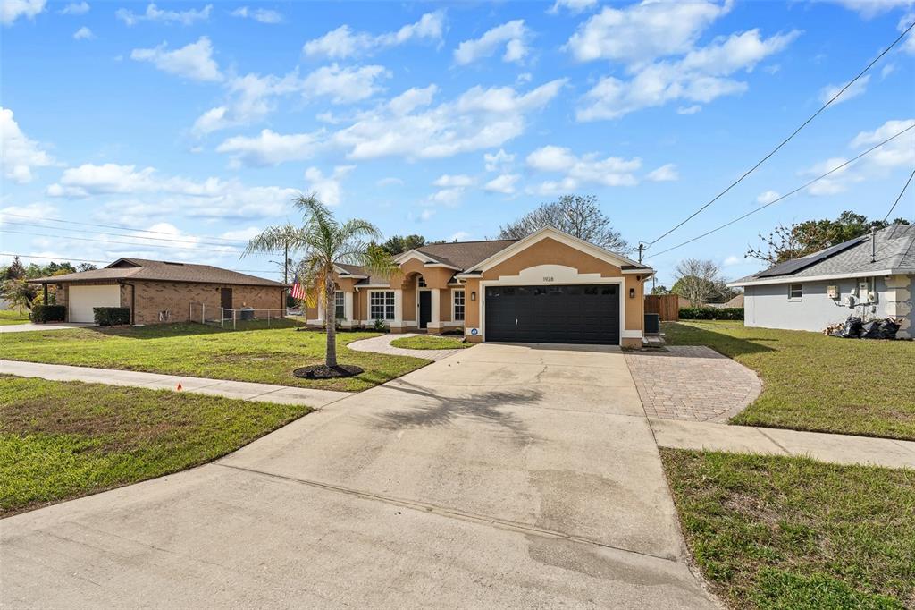 A tan, single-story house with a black garage door and a palm tree in front — 1928 EDEN DRIVE, DELTONA, FL