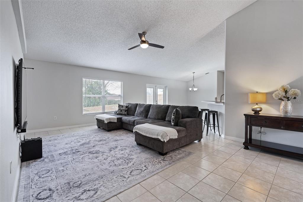 A living room features a gray sectional sofa, a large area rug, and tile flooring — 1928 EDEN DRIVE, DELTONA, FL