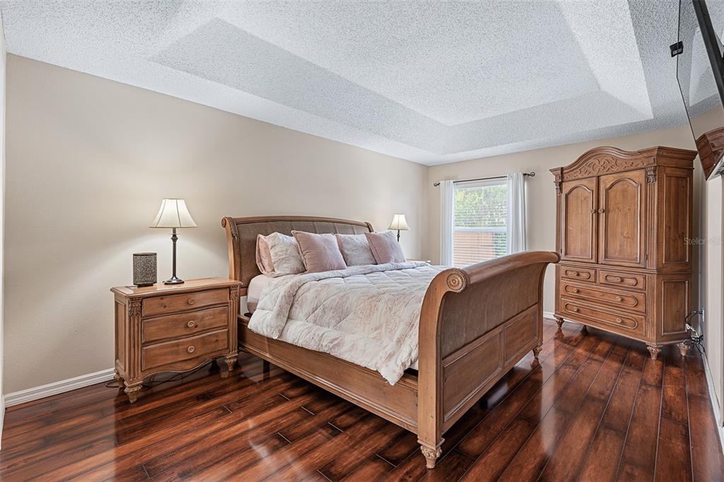 A bedroom features a wooden sleigh bed, matching furniture, and dark hardwood floors under a tray ceiling — 1928 EDEN DRIVE, DELTONA, FL