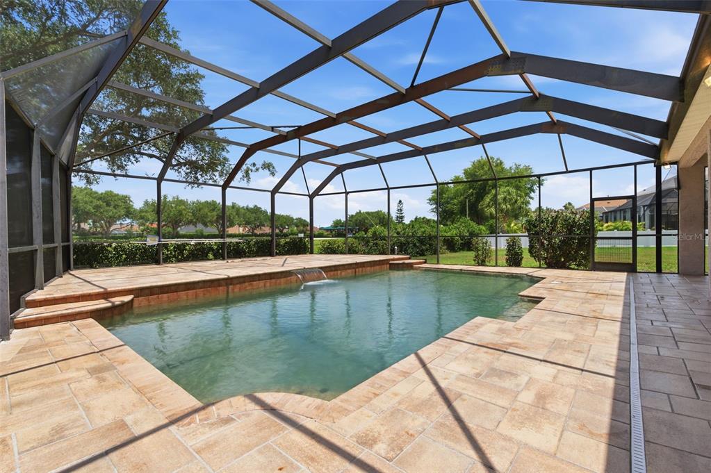A screened-in swimming pool with a stone deck and a small water feature — 1623 CROSSVINE COURT, TRINITY, FL