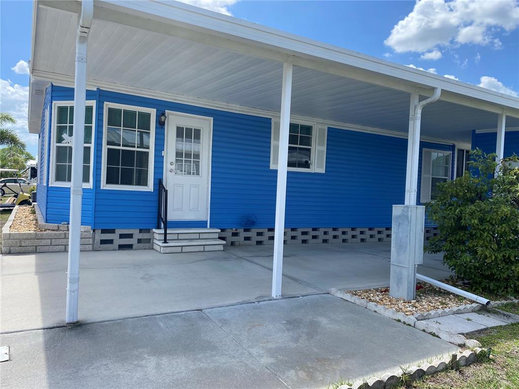 A blue mobile home features a white front door, a carport, and concrete block skirting — 701 RIVERVIEW CIRCLE, NORTH PORT, FL