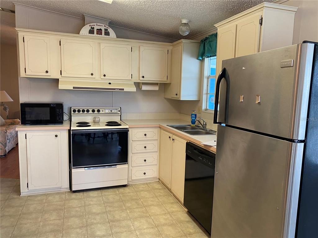 A kitchen features off-white cabinets, a stainless steel refrigerator, and a white electric range — 701 RIVERVIEW CIRCLE, NORTH PORT, FL