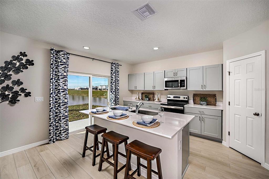 A kitchen with light gray cabinets, a quartz island, and a sliding door overlooking water — 15201 MAUDE LANDING LOOP, WIMAUMA, FL
