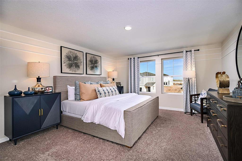 A bedroom features a gray upholstered bed, two dark dressers, and windows overlooking a construction site — 15201 MAUDE LANDING LOOP, WIMAUMA, FL