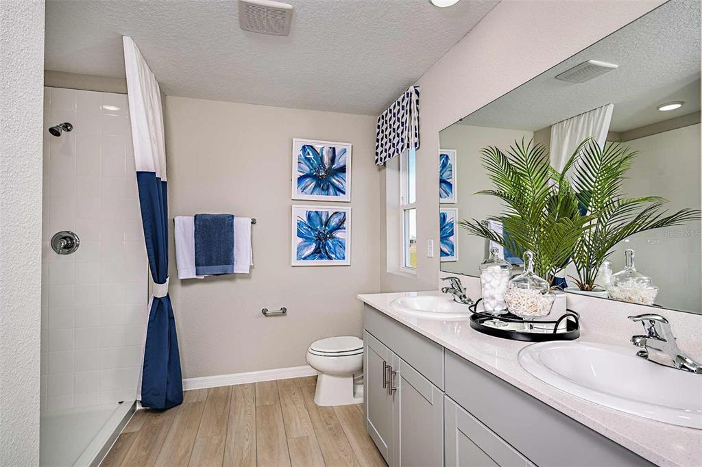 A bathroom features a double vanity, a walk-in shower, and blue-and-white floral wall art — 15201 MAUDE LANDING LOOP, WIMAUMA, FL