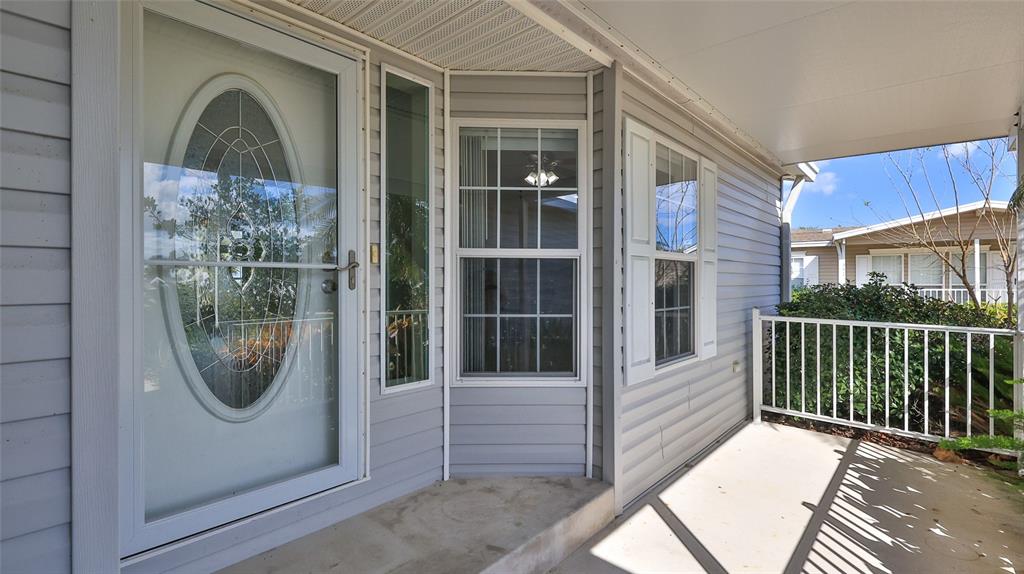 A covered porch with light gray siding, a glass storm door, and a white railing — 361 MARSH LANDING LOOP, OAK HILL, FL