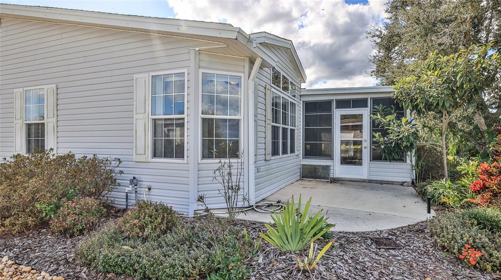 The exterior of a light-colored manufactured home features a screened-in porch and landscaped yard — 361 MARSH LANDING LOOP, OAK HILL, FL