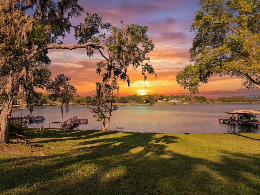 A grassy lawn overlooks a lake at sunset with two wooden docks and large trees — 2874 E CROOKED LAKE DRIVE, EUSTIS, FL
