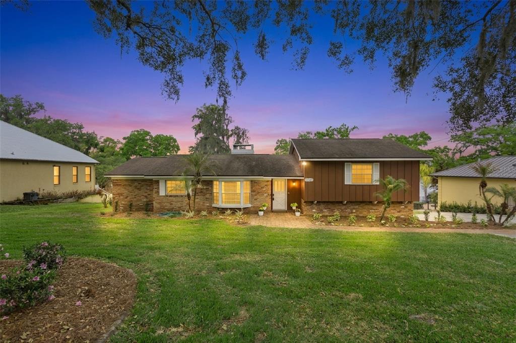 A single-story house with a brick and brown wood exterior sits on a grassy lawn — 2874 E CROOKED LAKE DRIVE, EUSTIS, FL