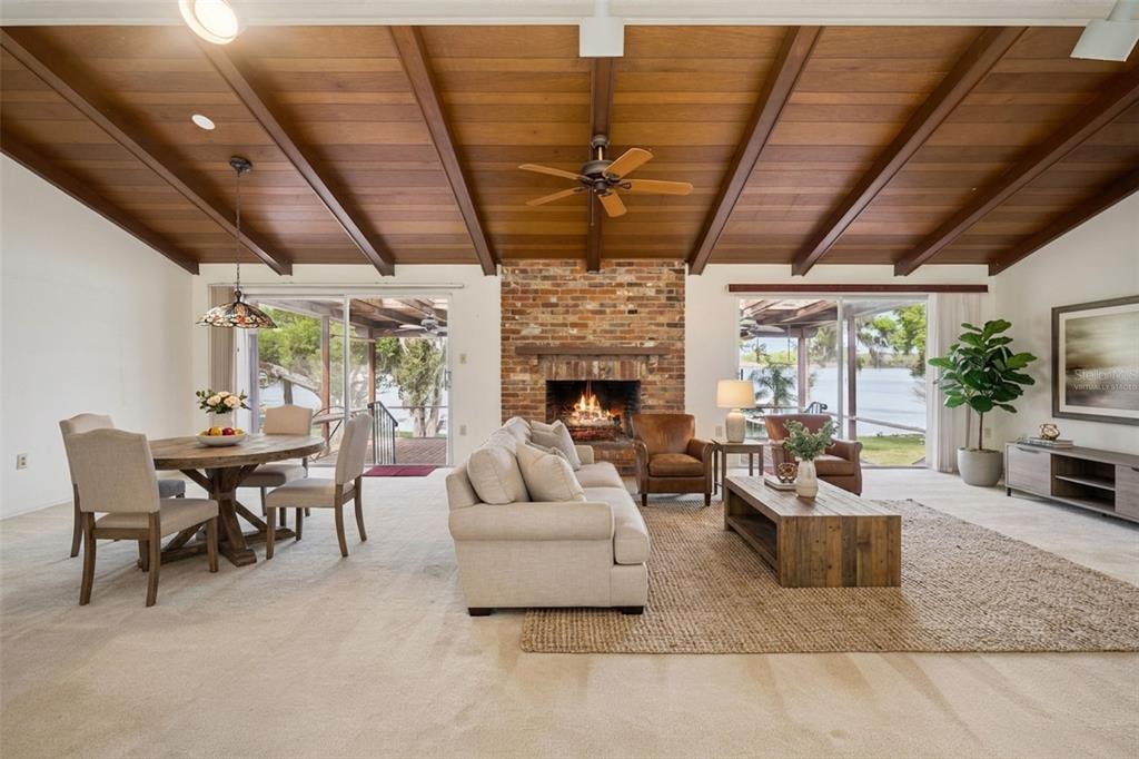 A living and dining room with a vaulted wood ceiling, brick fireplace, and sliding glass doors — 2874 E CROOKED LAKE DRIVE, EUSTIS, FL