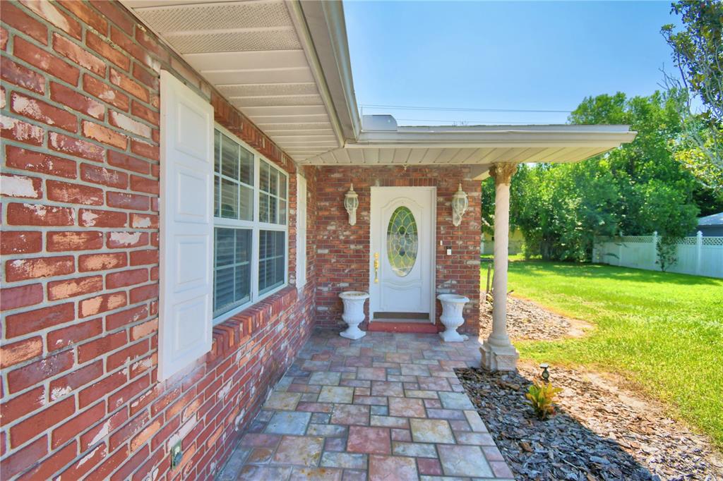 A brick house exterior features a covered front porch with stone pavers and a white door — 1206 SUSAN LANE, AUBURNDALE, FL