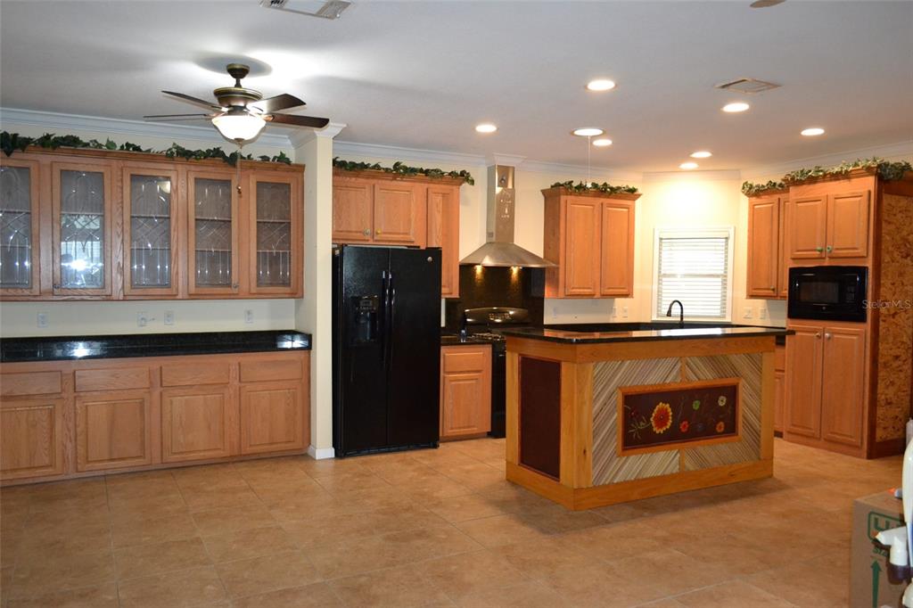 A kitchen features light wood cabinets, black countertops, a black refrigerator, and a central island — 3531 70TH AVENUE E, ELLENTON, FL