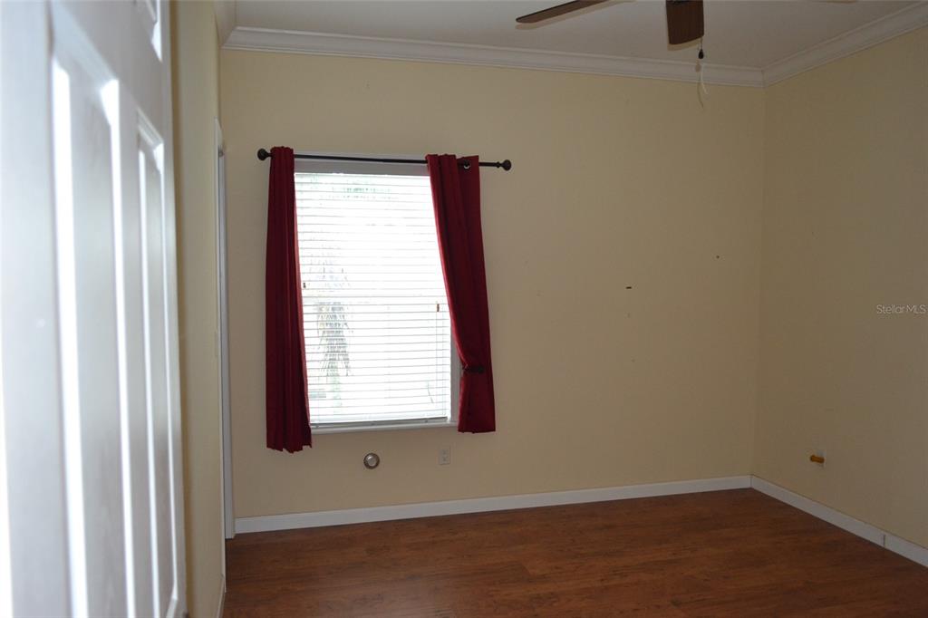 An empty bedroom with light yellow walls, wood-look flooring, a window with red curtains, and ceiling fan — 3531 70TH AVENUE E, ELLENTON, FL