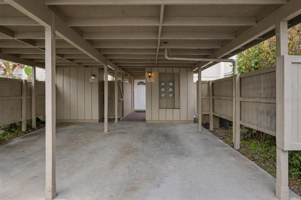 A covered carport with concrete flooring, wooden support beams, and two unit entrance doors — 7912 CEDAR DRIVE UNIT 7912, TEMPLE TERRACE, FL