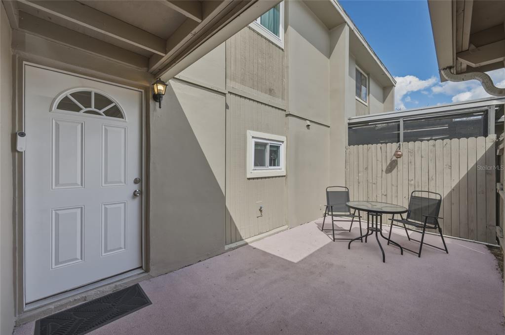 A white front door opens onto a small concrete patio with a table and chairs — 7912 CEDAR DRIVE UNIT 7912, TEMPLE TERRACE, FL