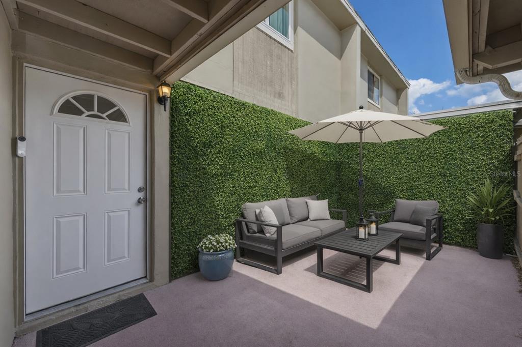 A patio features a white door, artificial hedge walls, outdoor furniture, and a patio umbrella — 7912 CEDAR DRIVE UNIT 7912, TEMPLE TERRACE, FL