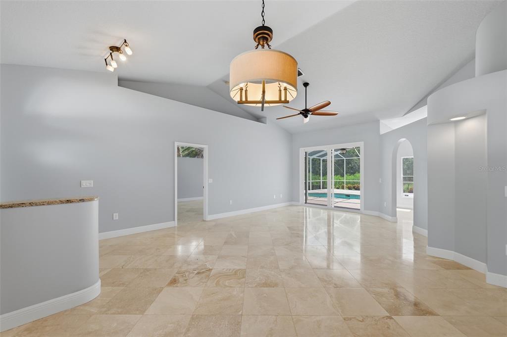 A spacious living room features light-colored tile flooring, a vaulted ceiling, and a large chandelier — 501 MANISHA PLACE, TARPON SPRINGS, FL