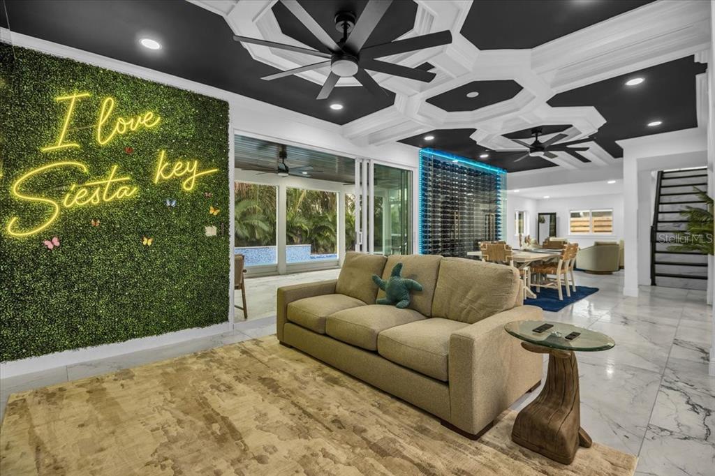 A living room features a green wall with neon signage, a sofa, and coffered ceilings — 5624 CAPE LEYTE DRIVE, SARASOTA, FL
