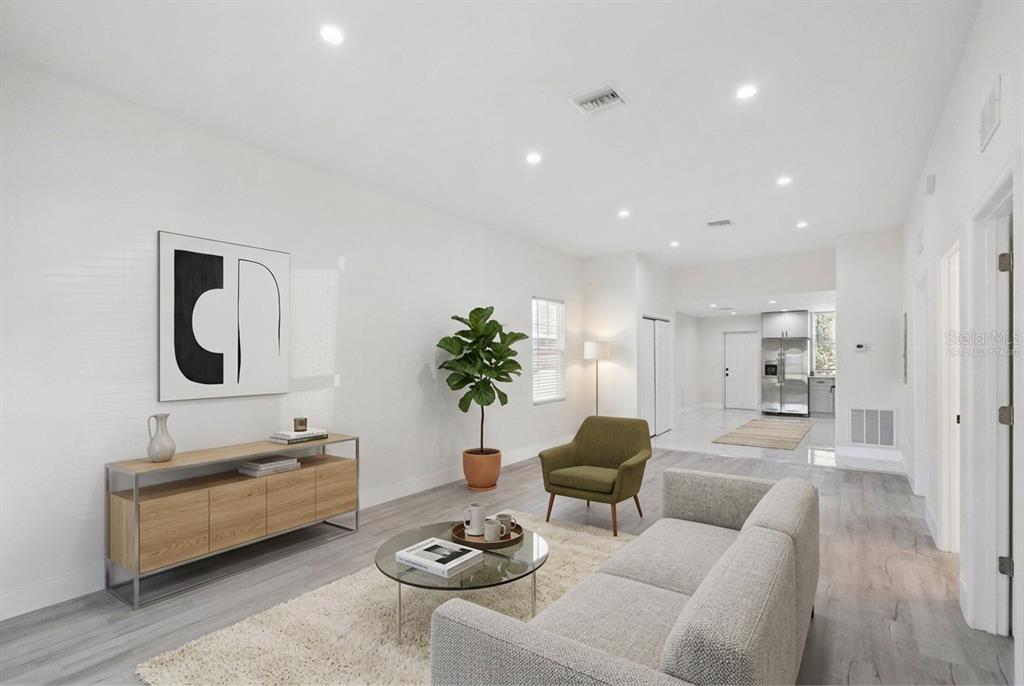 A living room with light wood flooring, a gray sofa, a green armchair, and white walls — 207 AVENUE E SE, WINTER HAVEN, FL