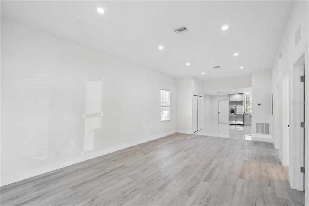 An empty room with light wood-look flooring, white walls, recessed lighting, and an adjacent kitchen — 207 AVENUE E SE, WINTER HAVEN, FL