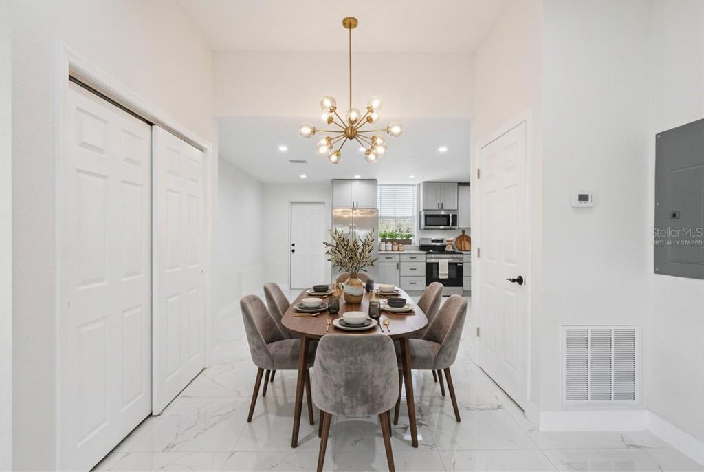 A dining area with a modern chandelier, oval table, and gray chairs on white tile floors — 207 AVENUE E SE, WINTER HAVEN, FL
