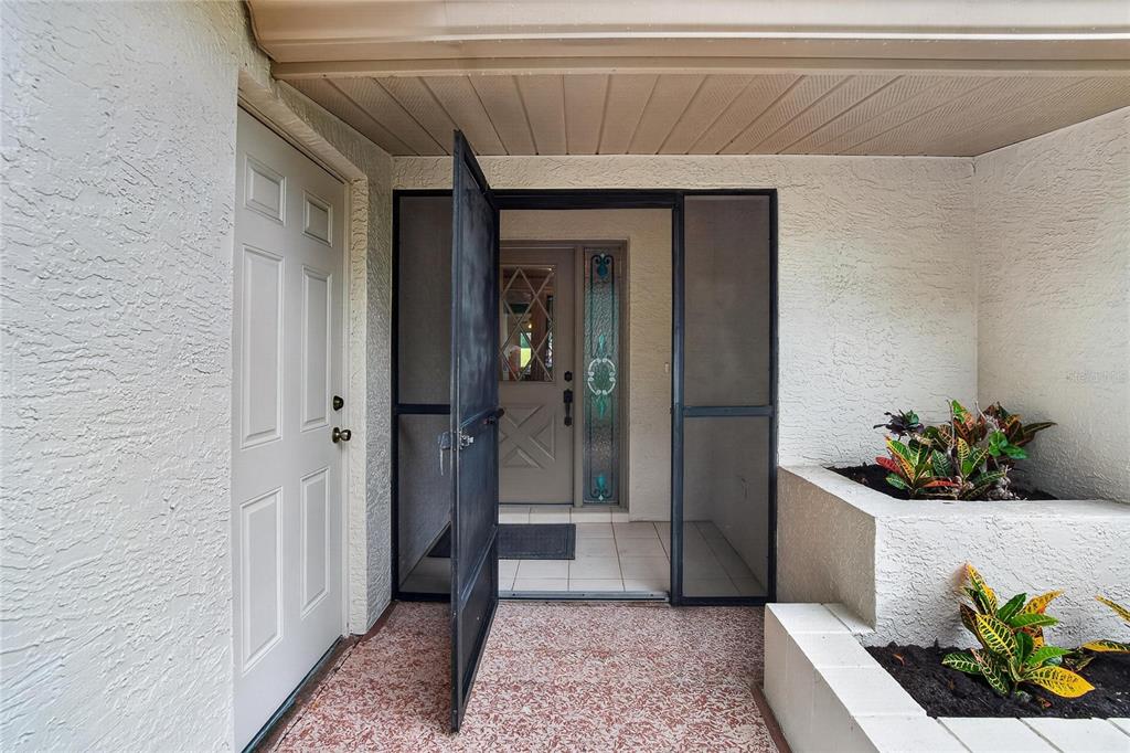 An exterior entryway features a white door, a screen door, and a tiered concrete planter — 1308 LELAND DRIVE UNIT 1308, SUN CITY CENTER, FL