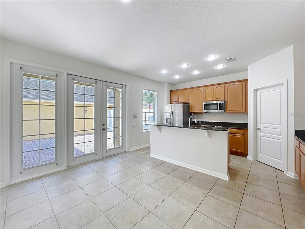 A kitchen with wood cabinets and a breakfast bar opens to a tiled dining area — 12930 VENNETTA WAY, WINDERMERE, FL