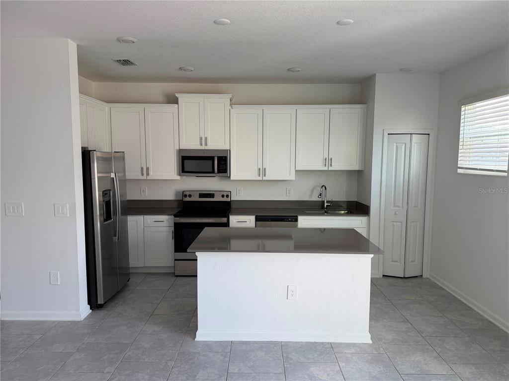 A kitchen features white cabinets, stainless steel appliances, a center island, and gray tile flooring — 7429 STONE CREEK TRAIL, KISSIMMEE, FL