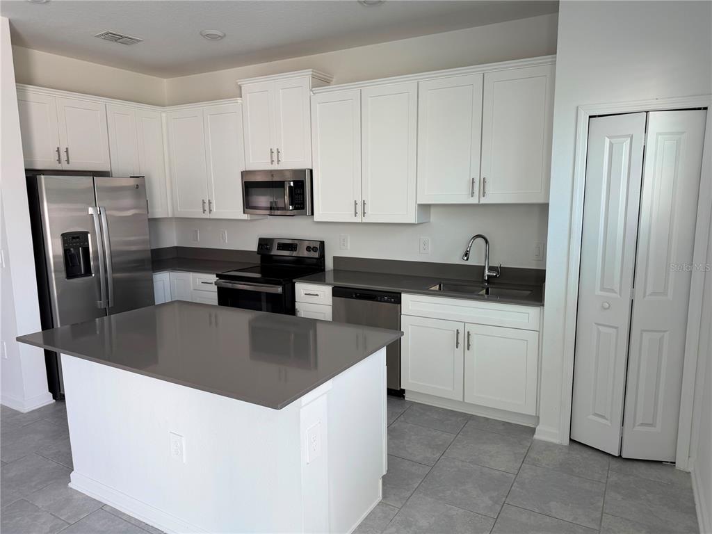A kitchen features white cabinets, gray countertops, stainless steel appliances, and a central island — 7429 STONE CREEK TRAIL, KISSIMMEE, FL
