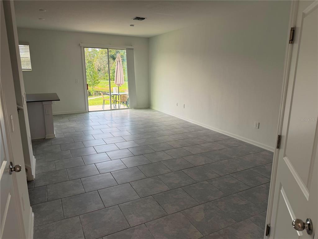 An empty room with gray tile flooring features a sliding glass door leading to a patio — 7429 STONE CREEK TRAIL, KISSIMMEE, FL